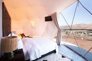 Ein Schlafzimmer mit einem großen Bett, einem Hängesessel, einer Lampe und Blick auf die Landschaft.