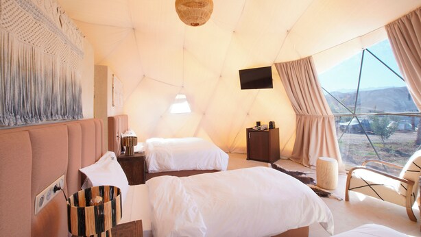 A tented accommodation room with two beds, a television, and a view of the outdoors.