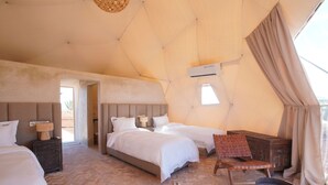 A tent-style room with two beds, a wooden chair, a small table, and a fur rug.