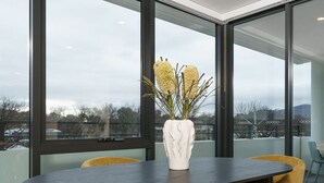 Ein moderner Essbereich mit einem runden Tisch, gelben Stühlen und einer weißen Vase mit gelben Blumen.