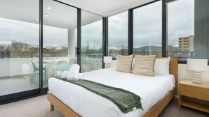 Et moderne soveværelse med en stor seng, udsigt over byen og en balkon med stole.
