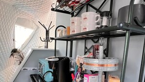 Une cuisine compacte dotée d’un plan de travail en bois, d’une étagère suspendue pour ranger les ustensiles de cuisine et d’un petit coin repas agrémenté de paniers en osier.
