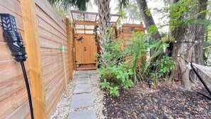 Une porte en bois avec un loquet en métal, un chemin de pierres et un hamac suspendu à un arbre.