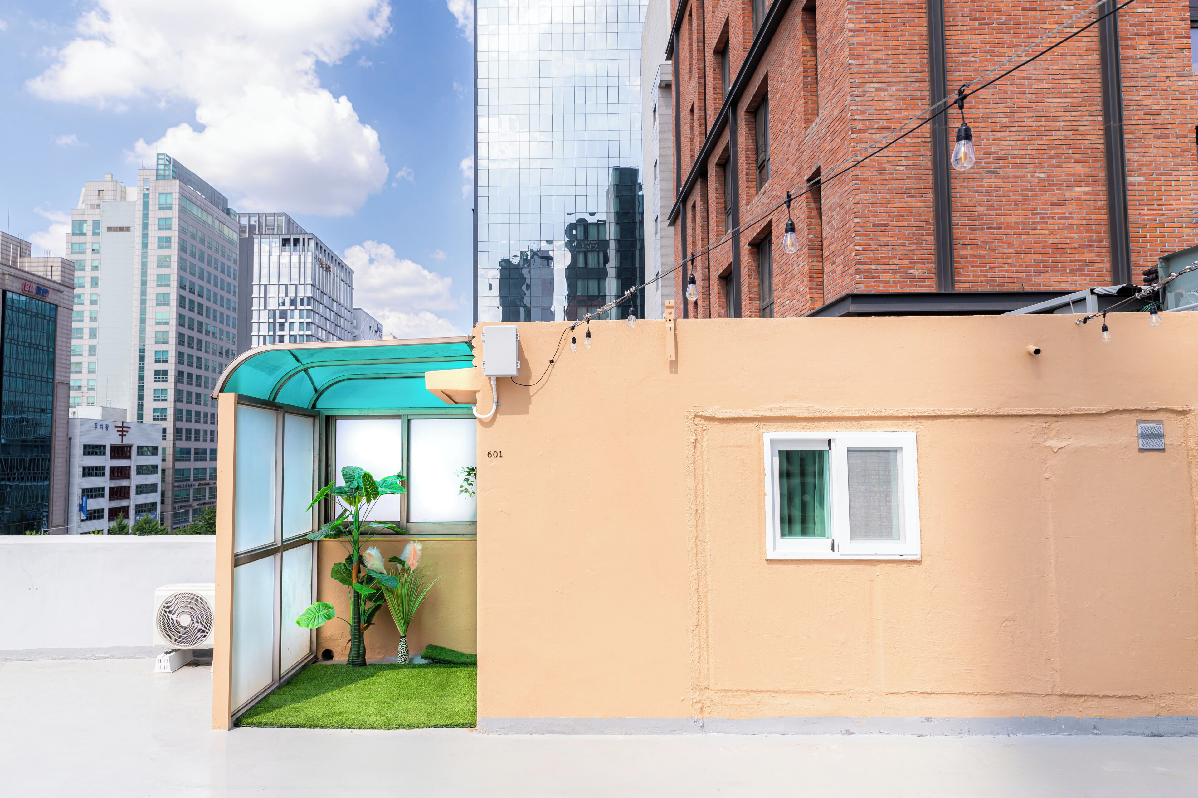 A modern building with a glass enclosure, a small garden, and a view of surrounding high-rise buildings.