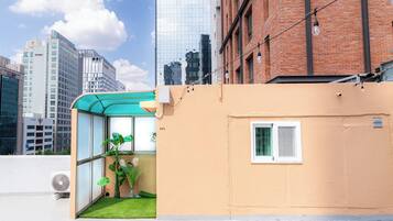 A modern building with a glass enclosure, a small garden, and a view of surrounding high-rise buildings.