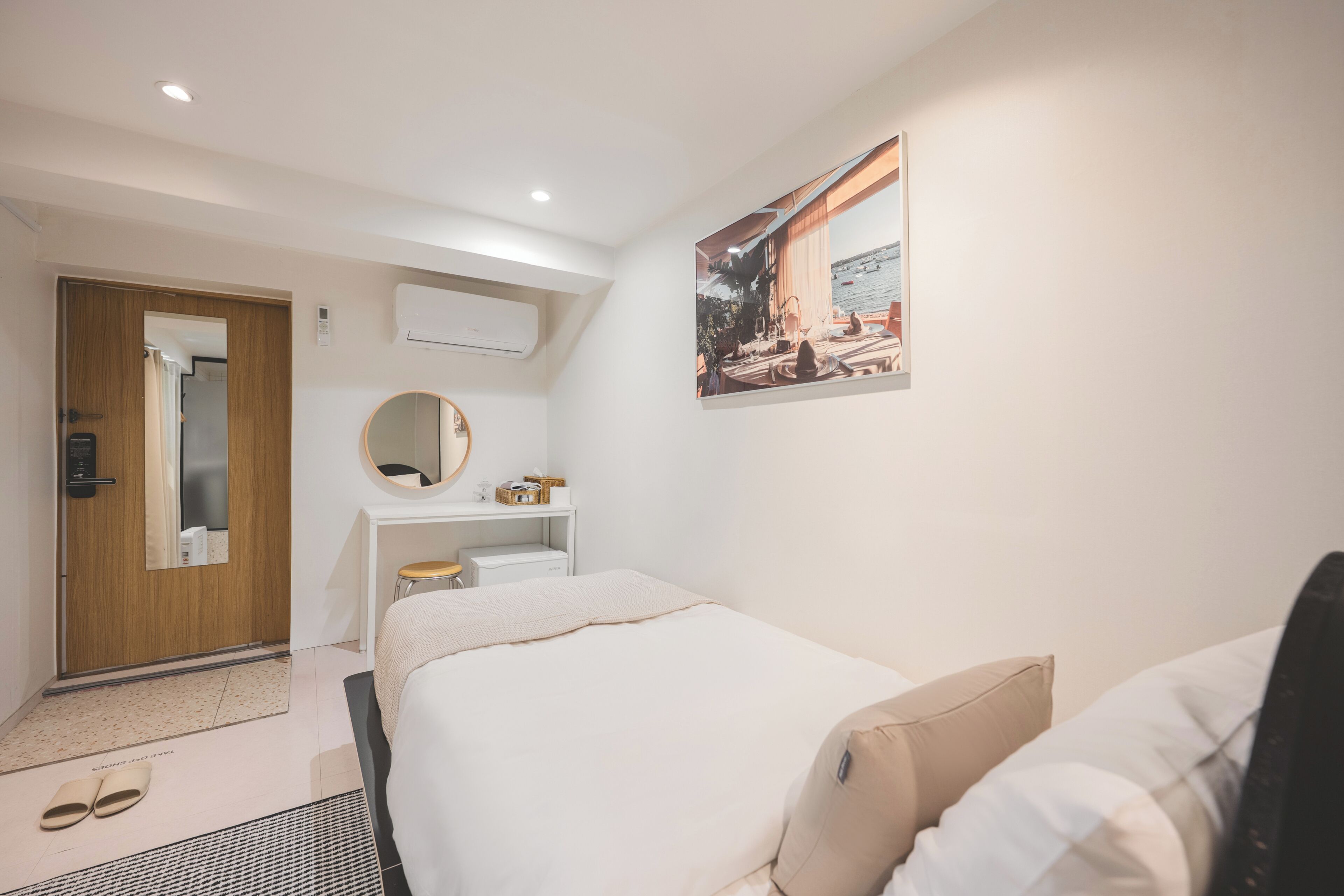 Quarto de hotel com cama, escrivaninha, espelho, quadro na parede e porta que dá para outro cômodo.