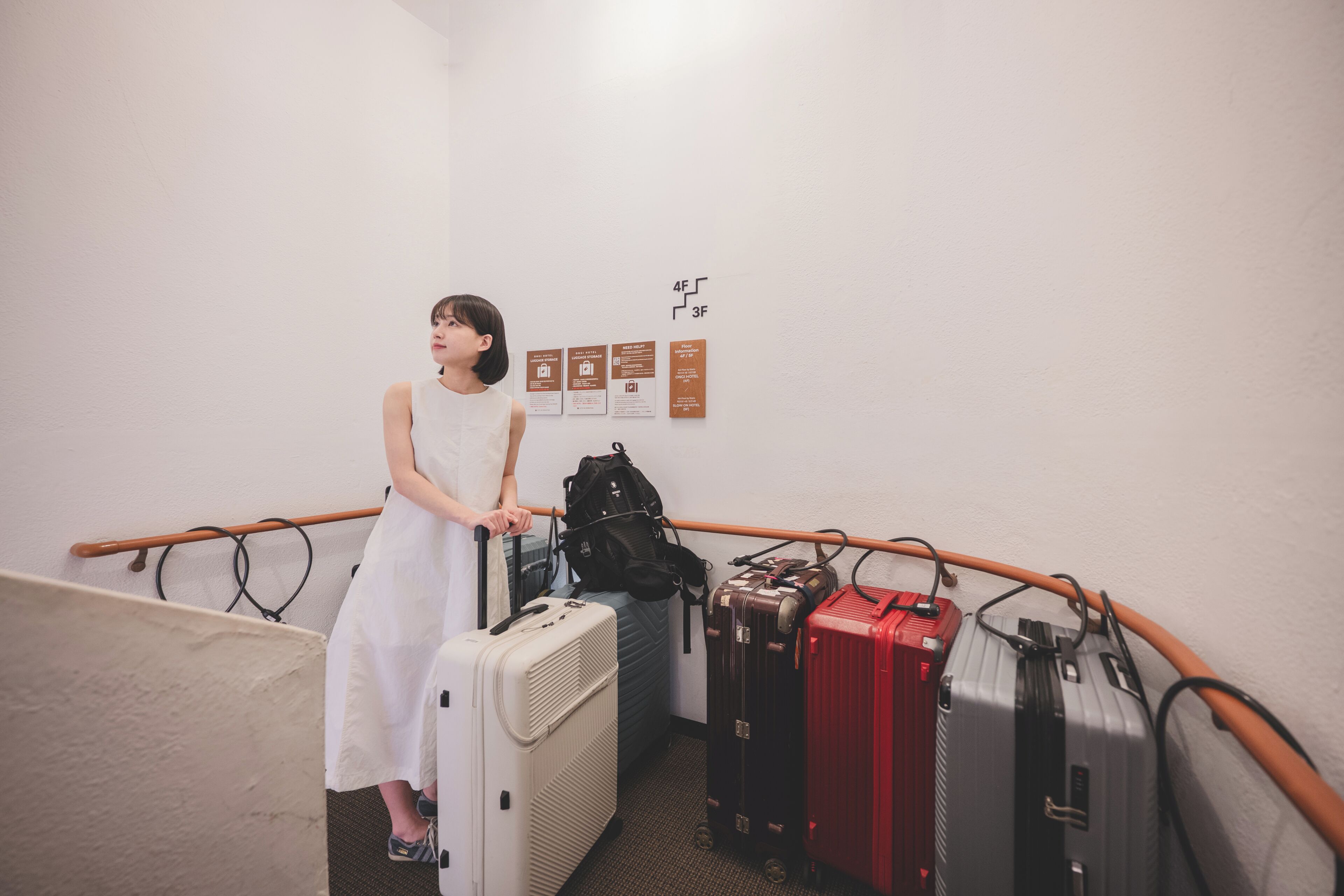 A person standing next to a luggage rack with suitcases, a wall with directional signs, and a wooden handrail.