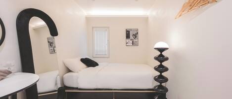 A bedroom with a bed, a desk, a chair, a mirror, a lamp, and a window.