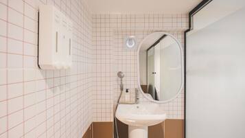 A bathroom with a white sink, a mirror, a handheld showerhead, and a soap dispenser.