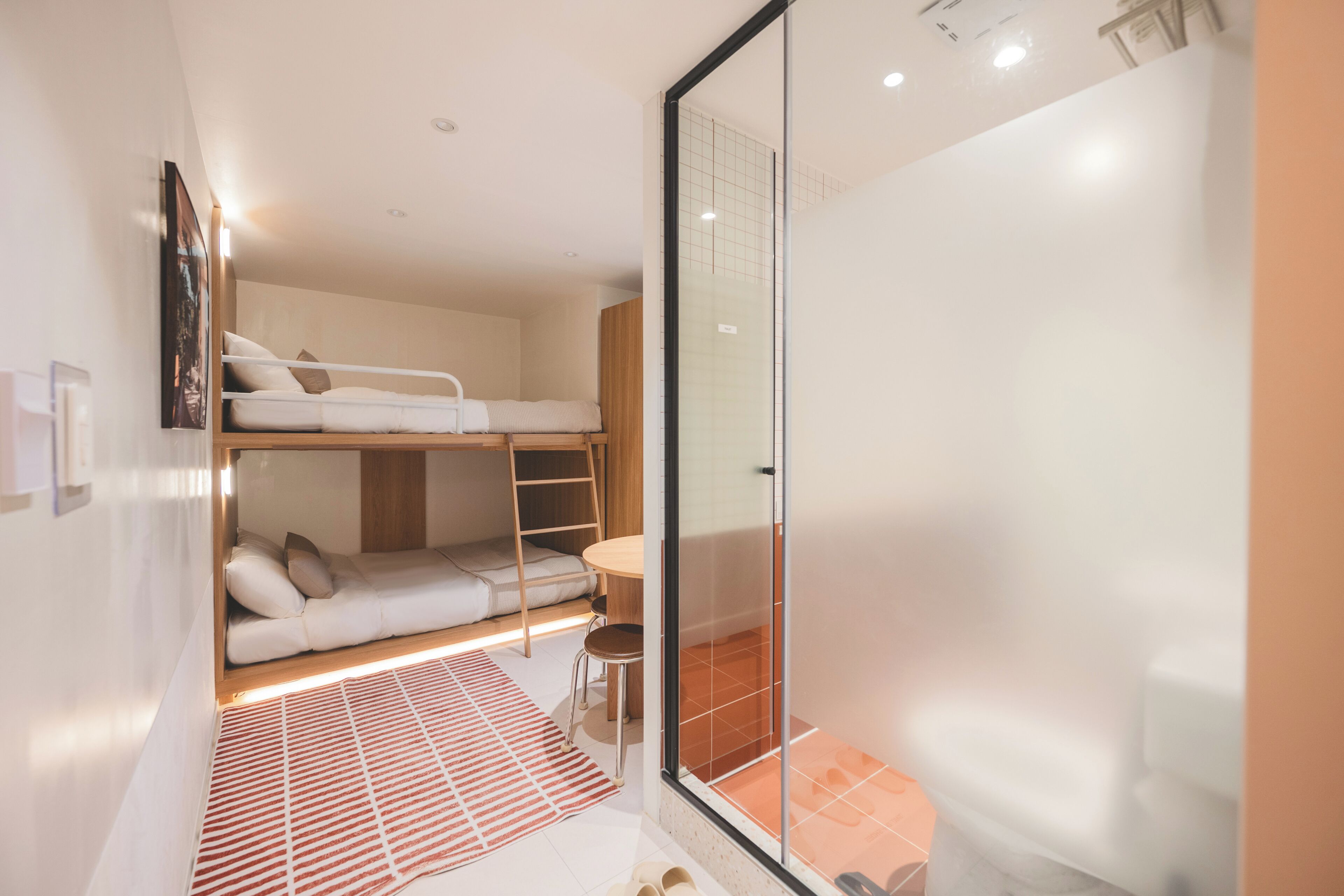 A compact room with a bunk bed, a small table, and a glass shower enclosure.