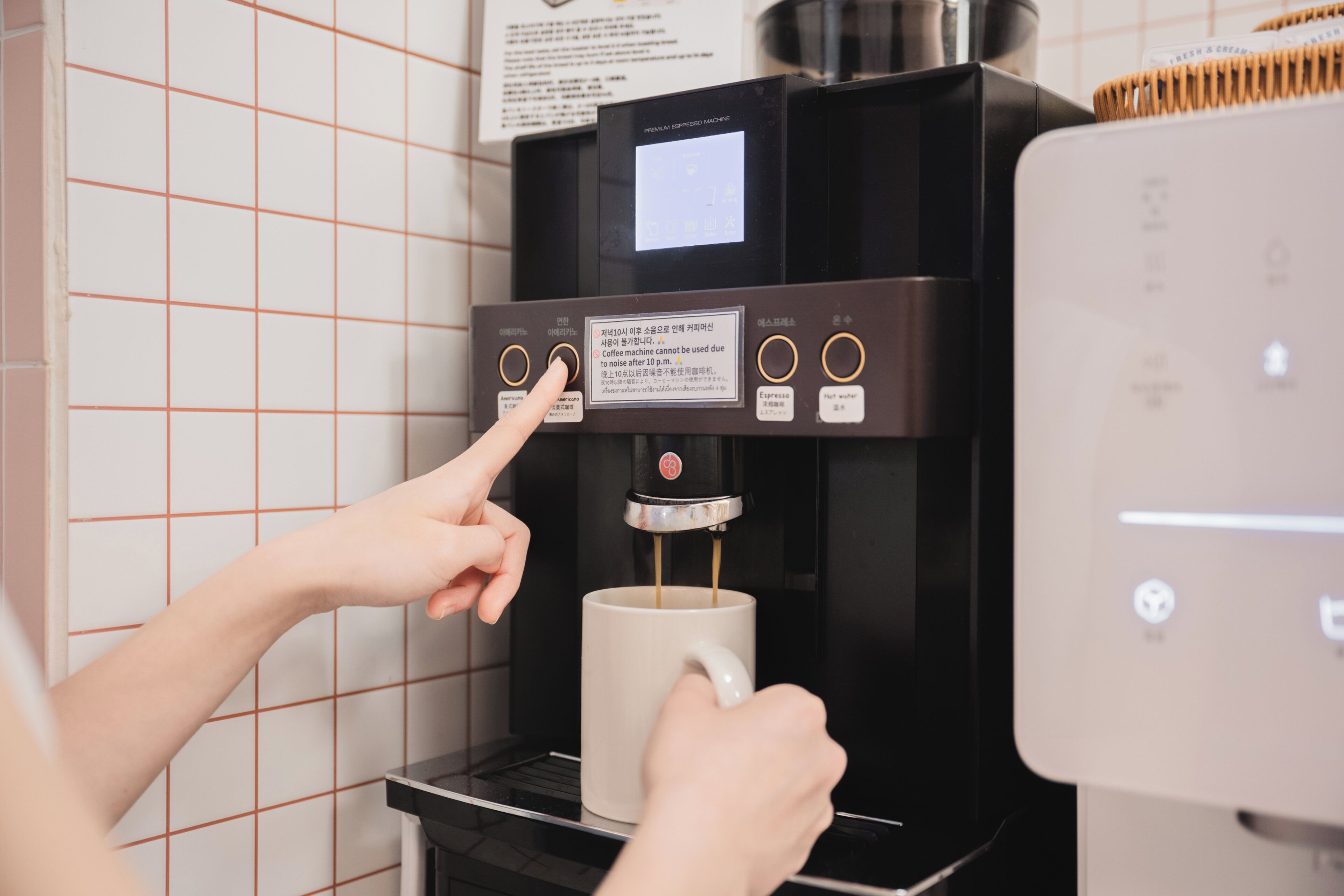 A person operating a coffee machine with a digital display, a coffee cup, and a control panel with buttons.
