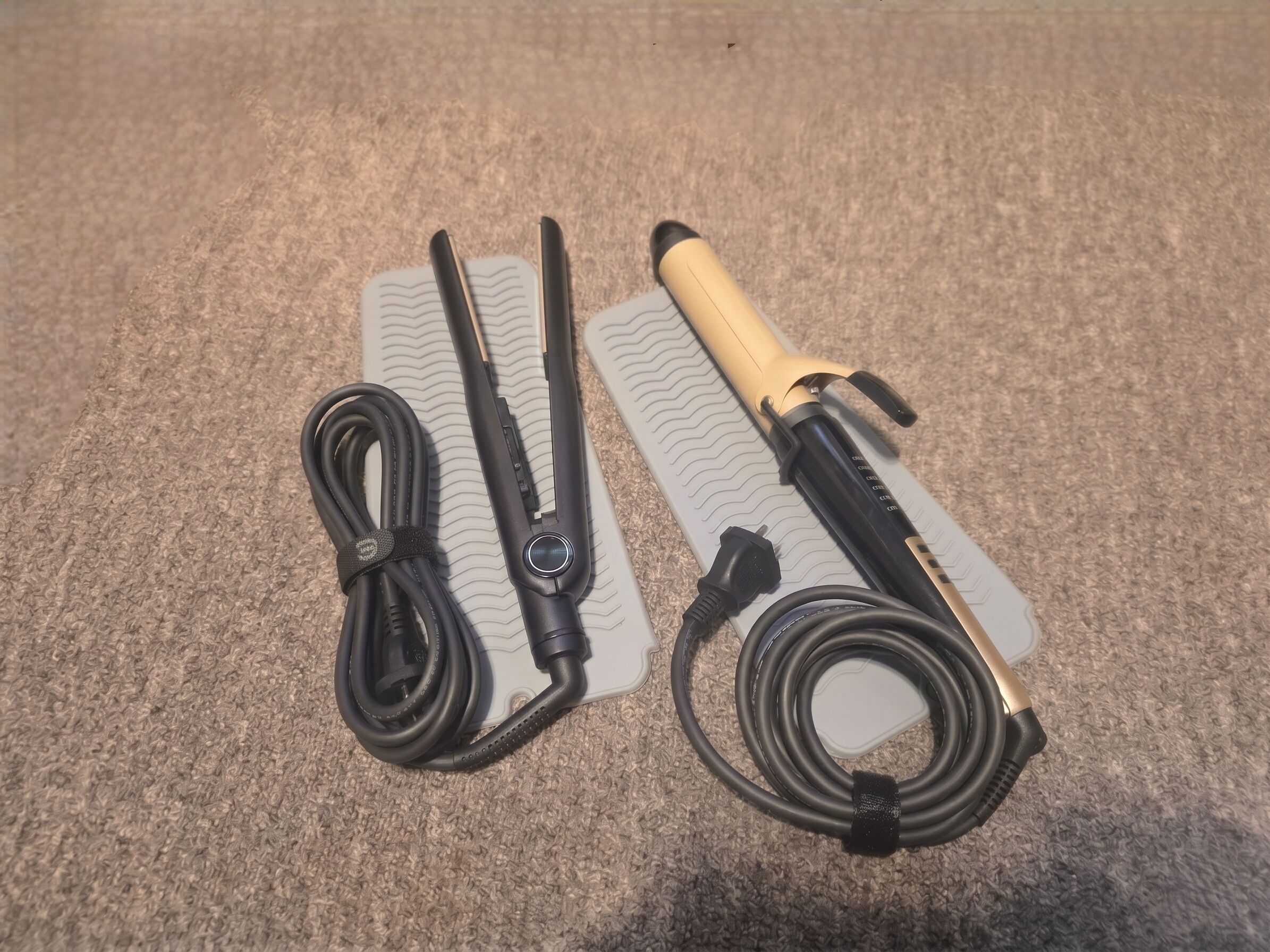 A flat iron, a hair straightener, and a hair clipper laid out on a textured surface.
