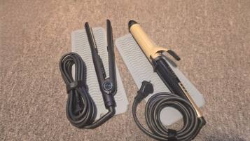 A flat iron, a hair straightener, and a hair clipper laid out on a textured surface.