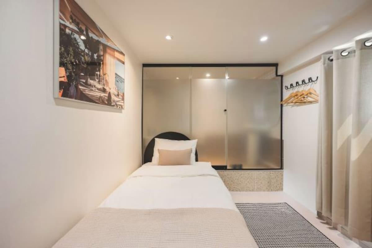 Quarto de hotel moderno com cama, área de chuveiro e vista para o exterior.