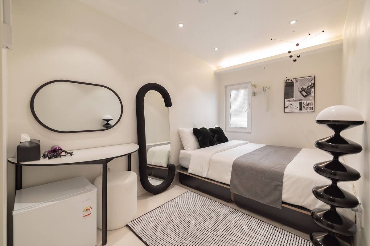 Un dormitorio moderno con cama, mesita de noche, espejo y ventana.