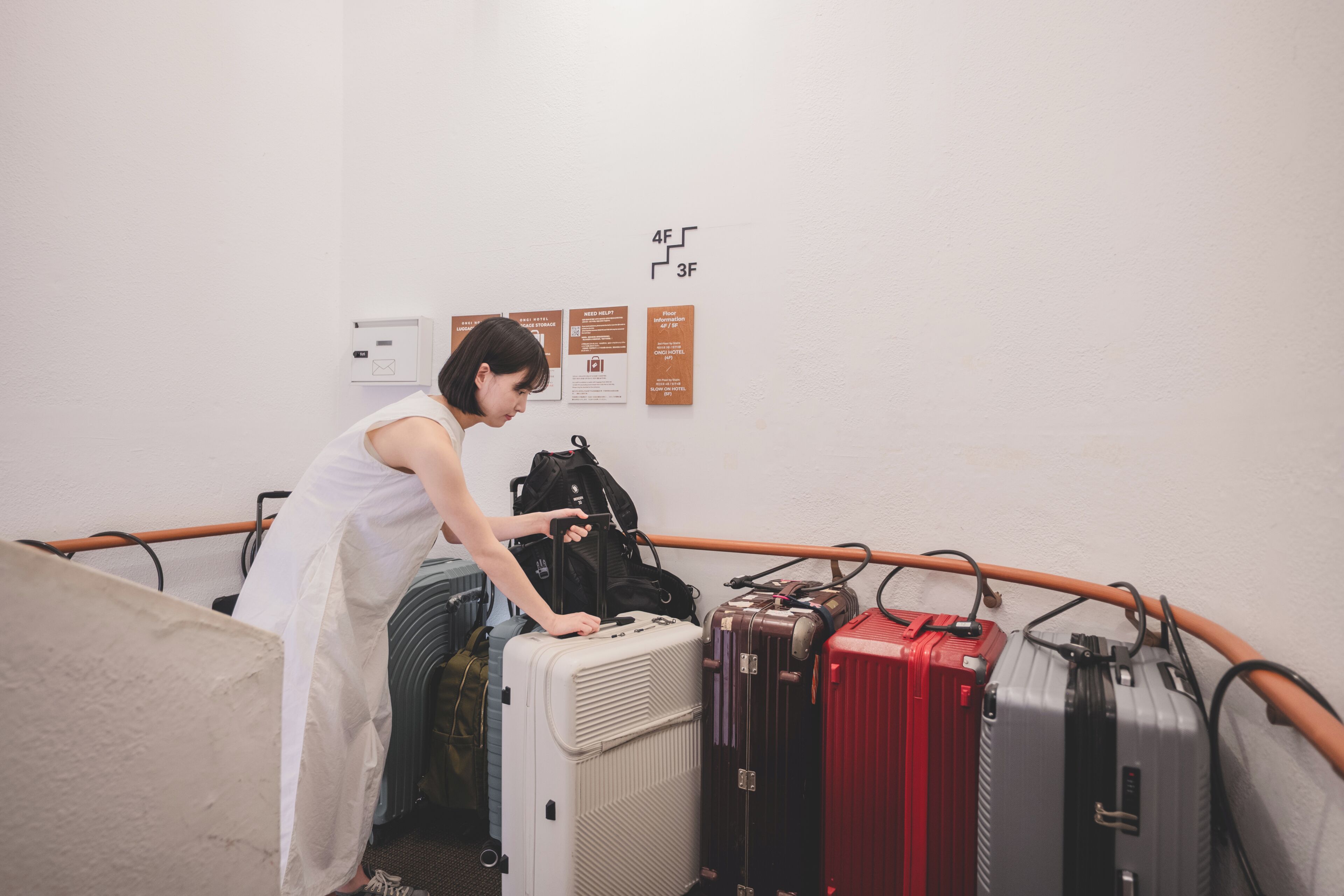 A person arranging luggage in a room with a white wall, a wooden railing, and informational signs.
