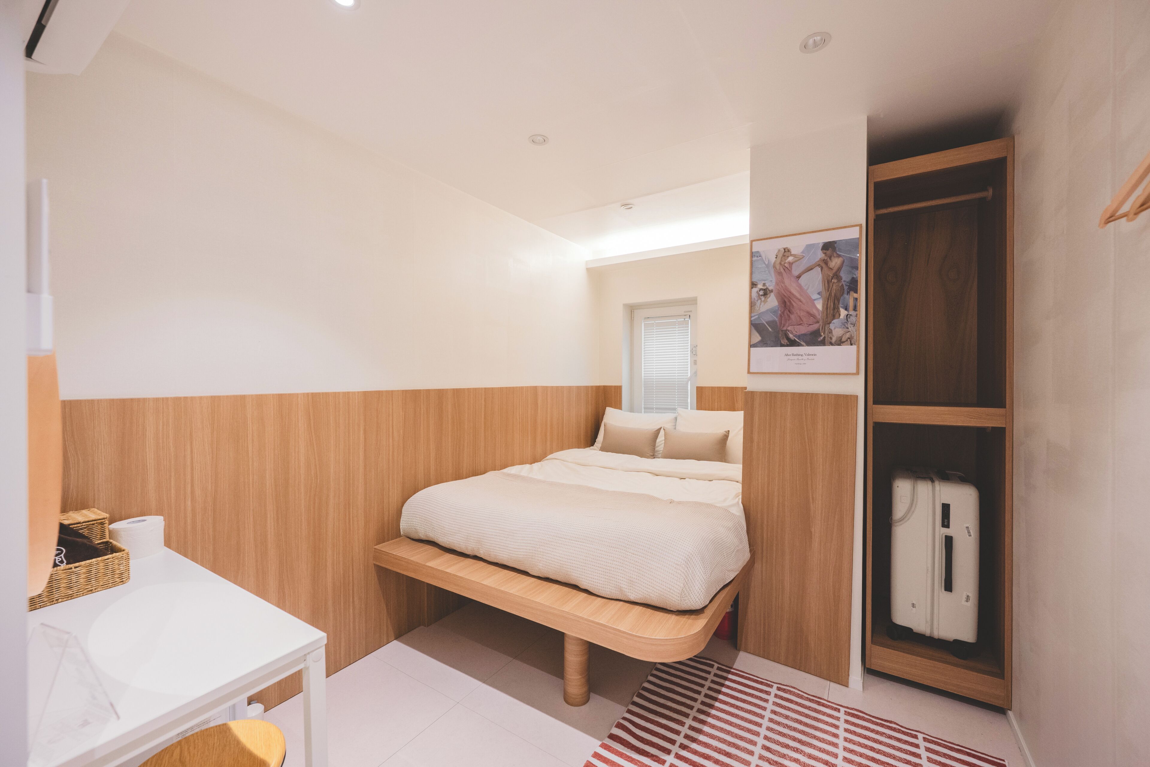 A bedroom with a bed, a wardrobe, a small table, and a window.