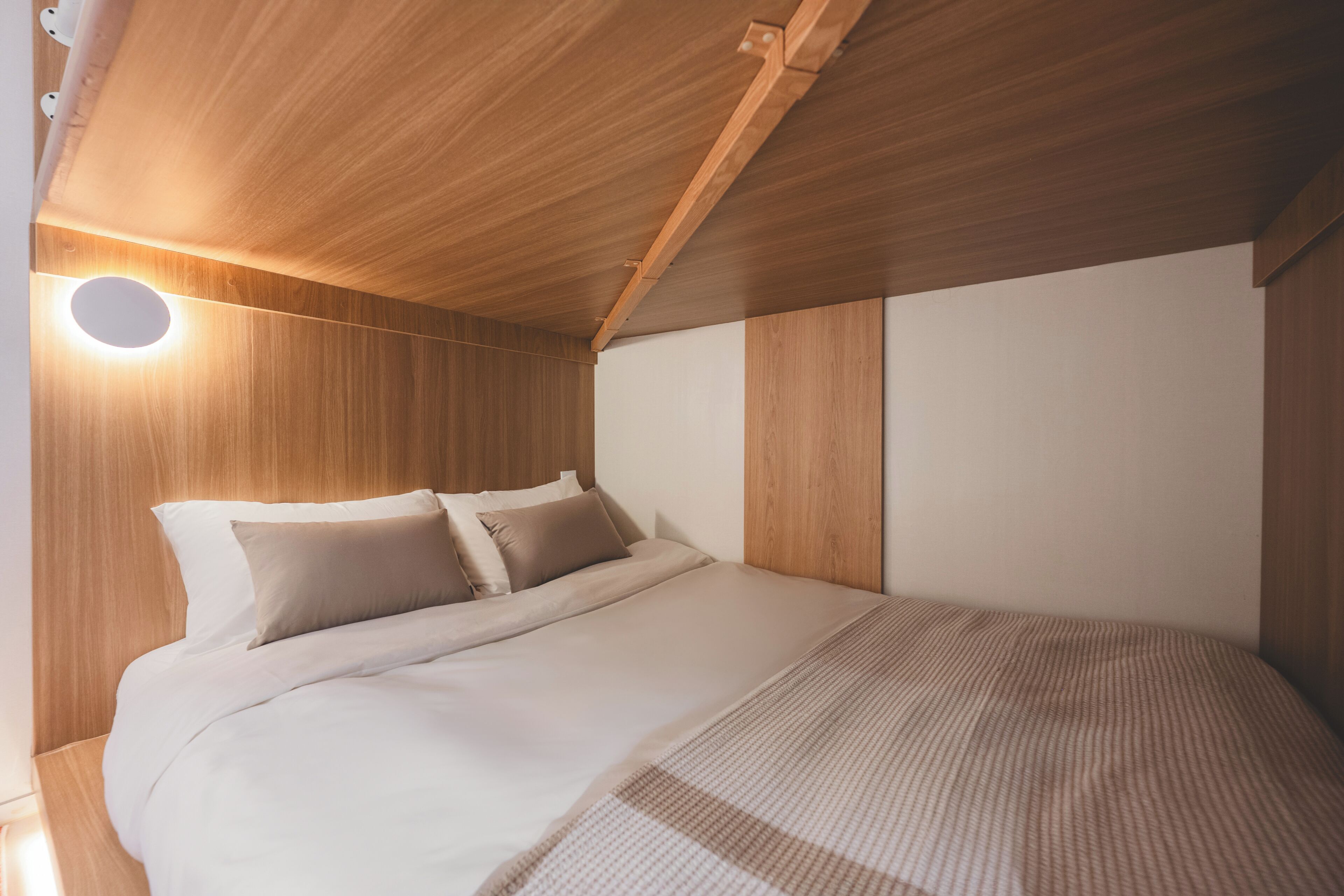 A bedroom with a wooden ceiling, a bed with white bedding, and a circular light fixture.