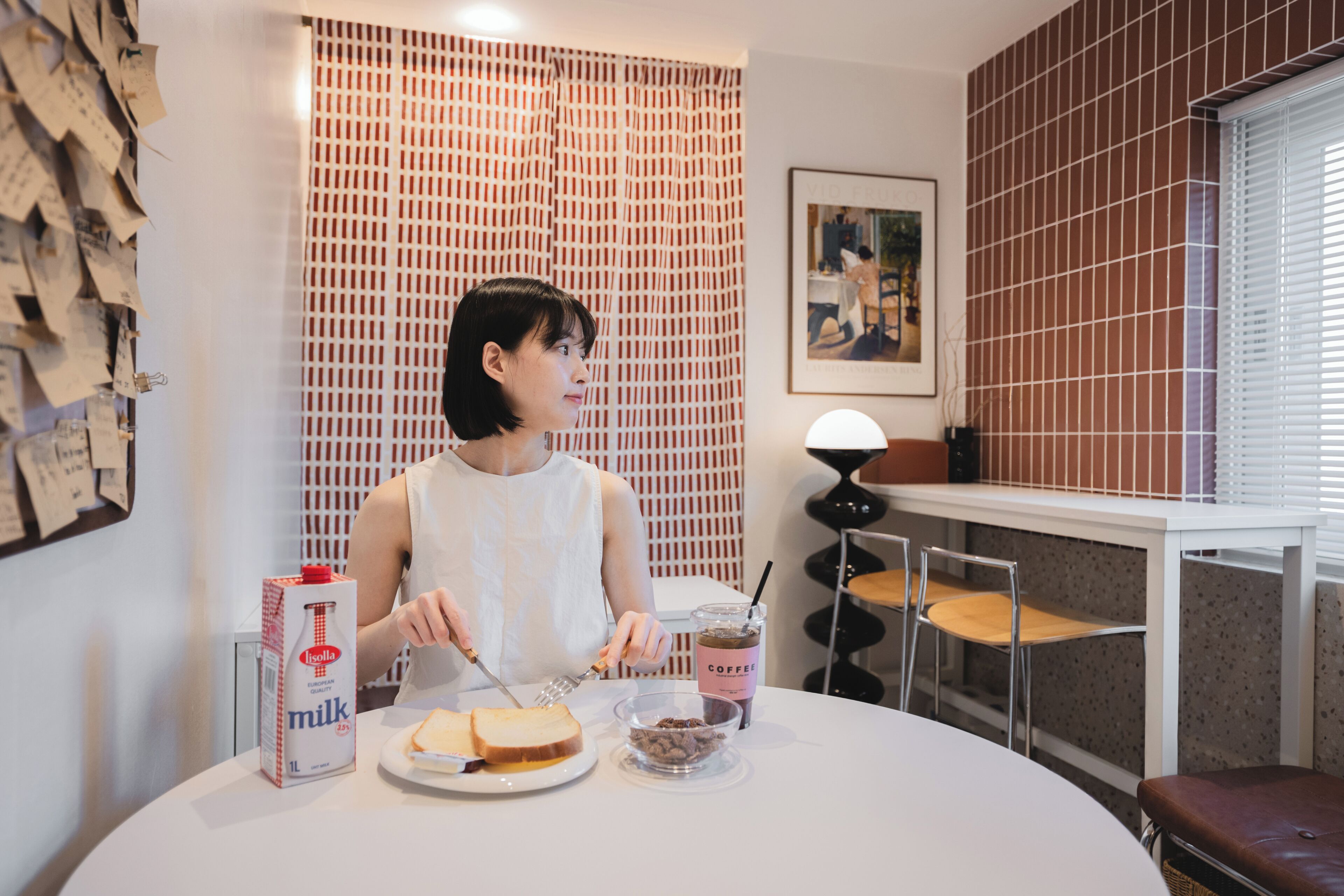 A person cutting bread at a table with a milk carton, a coffee cup, and a bowl of chocolate chips.
