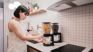 A person using a coffee machine in a kitchen with a tiled backsplash and wooden cabinets. - Slowon Hongdae (Seoul)