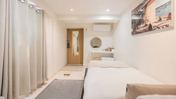 A hotel room with a bed, a desk with a mirror, a small stool, a window with a view of the sea, and a door leading to another room.
