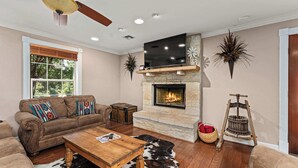A living room with a stone fireplace, leather sofa, wooden coffee table, and a ceiling fan.