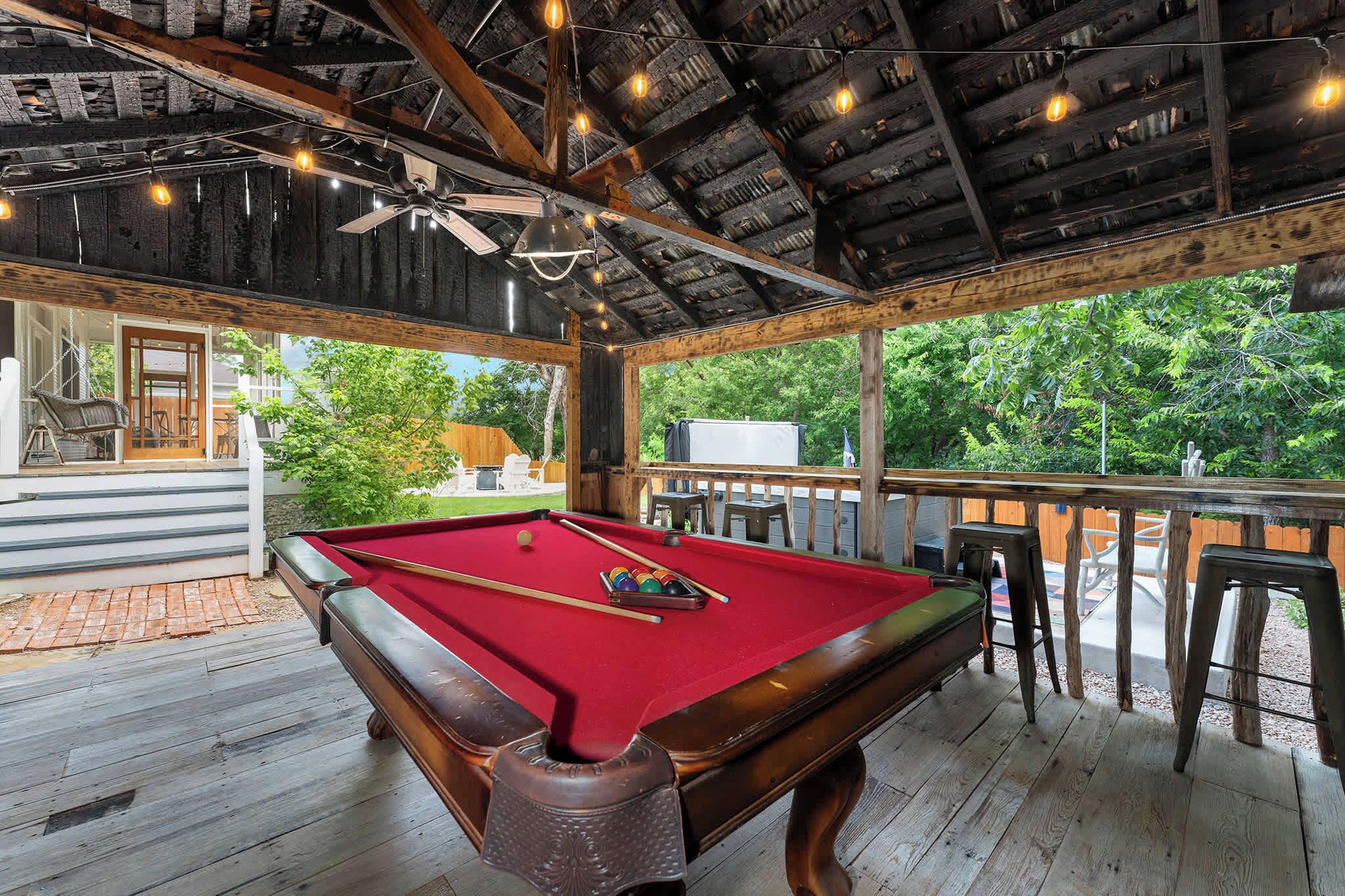 Une table de billard recouverte d’un feutre rouge, entourée de bois, et offrant une vue sur la verdure à l’extérieur.