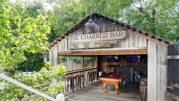 A wooden bar structure with a sign reading 'The Charred Bar,' a pool table, and bar stools.