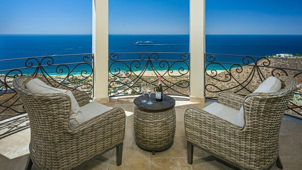 Un balcón con muebles de mimbre y una mesa, con vistas a una playa y al mar.