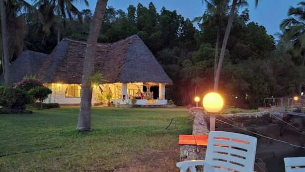 A thatched-roof building with a well-lit outdoor area, surrounded by palm trees and greenery. - Villa bonito (Mombasa)