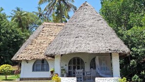 A thatched-roof hut with a white exterior, arched windows, and a small porch area. - Villa bonito (Mombasa)