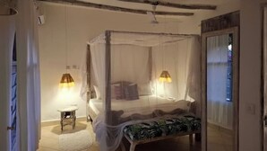 A bedroom with a four-poster bed, a bedside table, and two wall-mounted lamps. - Villa bonito (Mombasa)