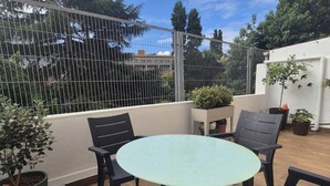 A patio with a round table and chairs, surrounded by potted plants and a metal fence.