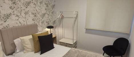 A bedroom with a bed, a bedside table with a lamp, a chair, and a window.