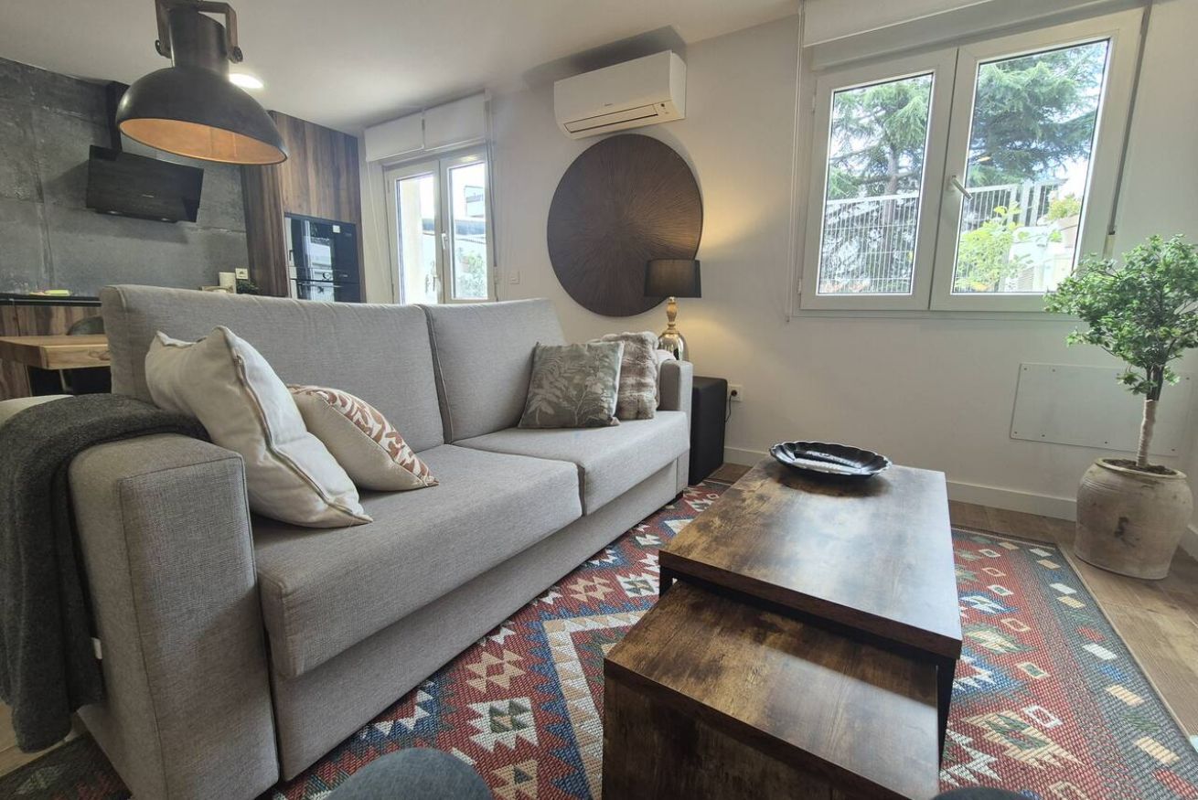 Una sala de estar moderna con un sofá gris, una mesa de centro de madera y una alfombra estampada.
