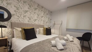 A hotel room with a bed, a nightstand, a chair, a mirror, and a window.