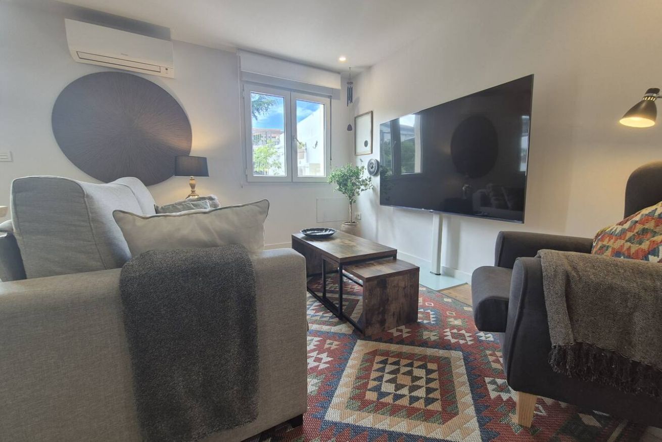 A living room with a sofa, a coffee table, a TV, and a patterned rug.