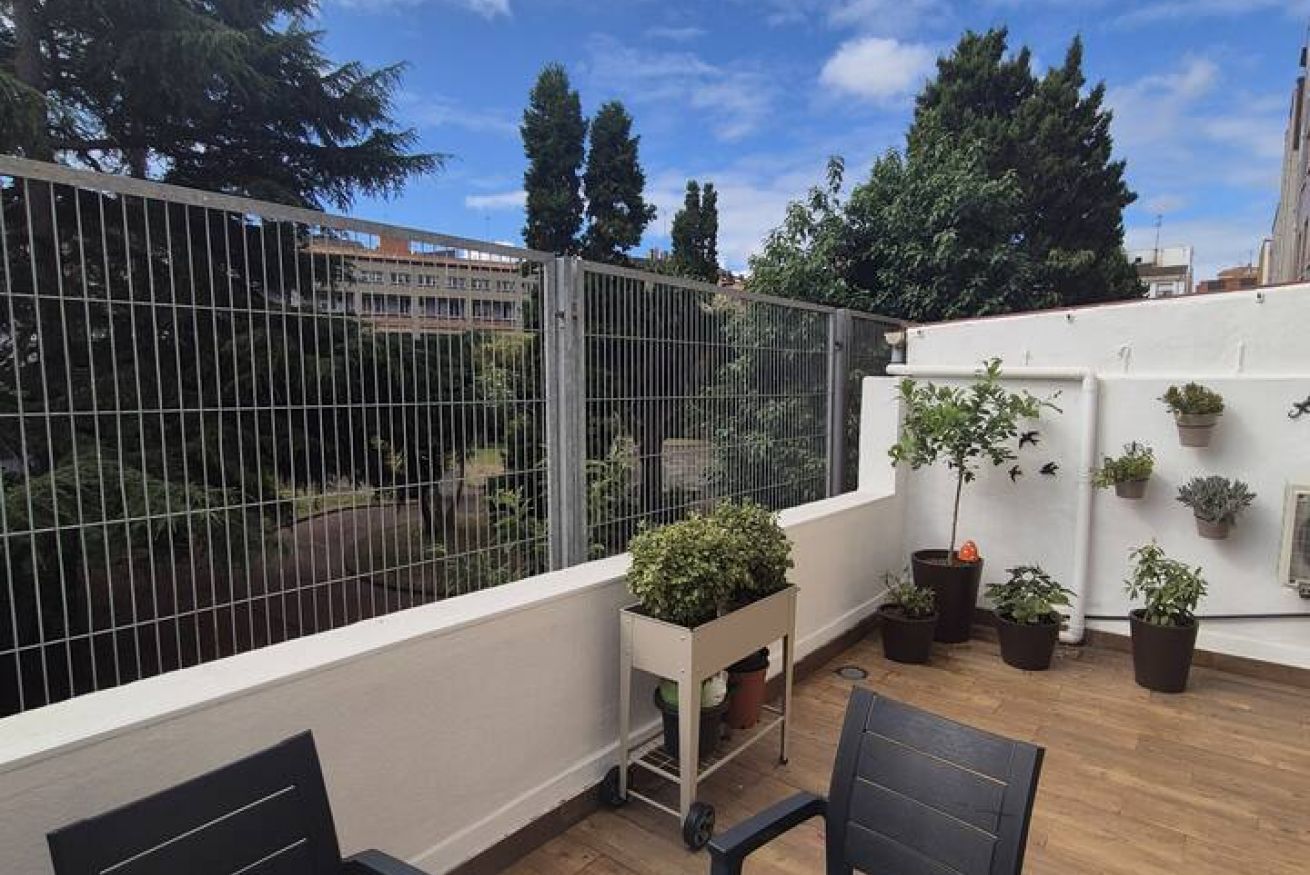 Un balcón con barandilla de metal, macetas con plantas y vistas a árboles y edificios.