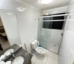 A modern bathroom with white tiles, a granite countertop, two sinks, a toilet, and a glass-enclosed shower. - Lacqua diRoma (Caldas Novas)