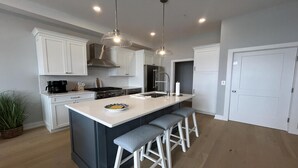 A modern kitchen with white cabinetry, a central island with bar stools, a stainless steel range, and pendant lighting. - Brand new Bayfront Luxury Townhome with Pool and Elevator. (Spray Beach)