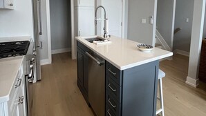 A modern kitchen with a central island, white cabinetry, and a stainless steel range hood. - Brand new Bayfront Luxury Townhome with Pool and Elevator. (Spray Beach)