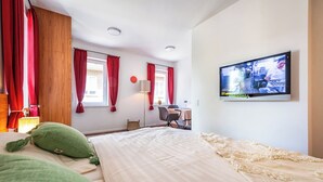 A hotel room with a bed, a desk, a chair, a television, and red curtains.