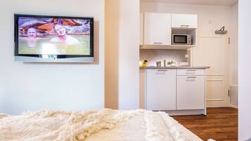 Een slaapkamer met een bed, een televisie aan de muur en een kitchenette met kastjes en een magnetron.