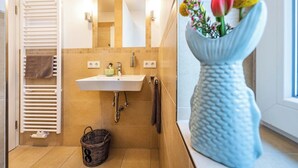 A bathroom with a white sink, mirror, towel rack, and a decorative vase with flowers.