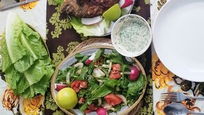 Ein Tisch ist reichhaltig mit Speisen gedeckt, darunter gebratener Fisch, Pommes, Salat und Fladenbrot.