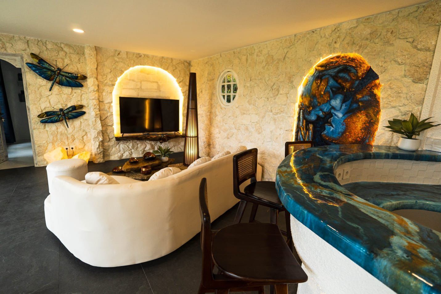 A spa area with a curved hot tub, a seating area with a fireplace, and decorative dragonfly wall art.