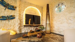 A stone-walled room with a fireplace, decorative dragonflies, a round window, and a zebra-patterned rug. - Villa AZUR (Bali)