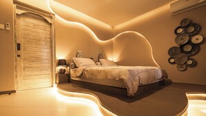 A bedroom with a curved bed, bedside tables, a wall-mounted lamp, and a decorative wall piece. - Villa AZUR (Bali)
