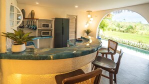 A kitchen with a marble countertop, a refrigerator, a microwave, and a toaster oven. There is a window with a view of a garden. - Villa AZUR (Bali)
