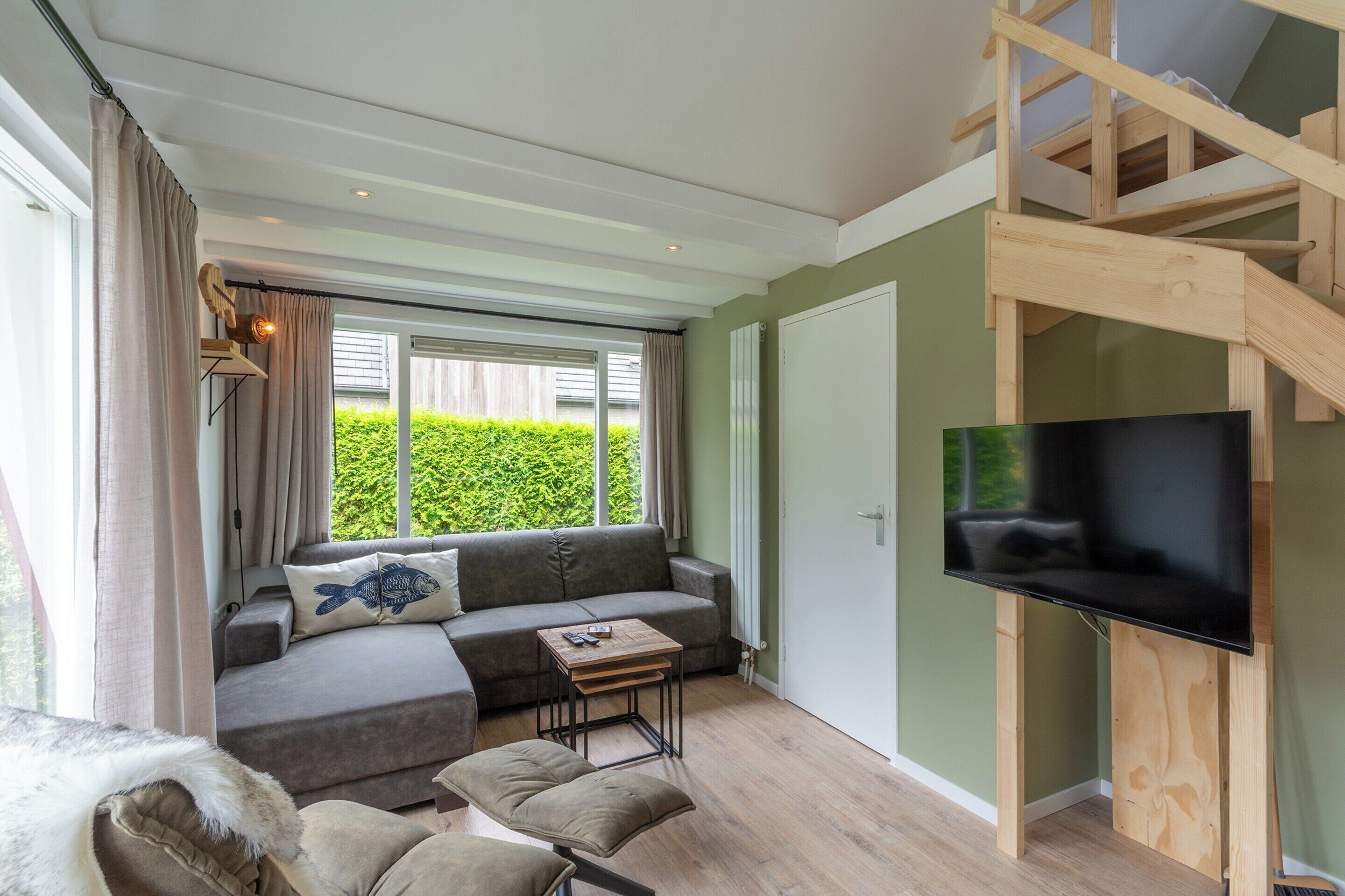 A modern living room with a grey sectional sofa, a wooden TV stand, and a staircase.
